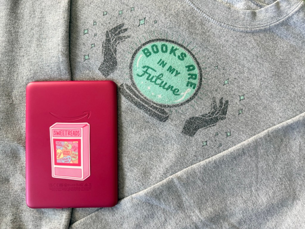 A photo of a pink Kindle paper white lying on a crewneck sweatshirt that reads: “Books are in my future.”
